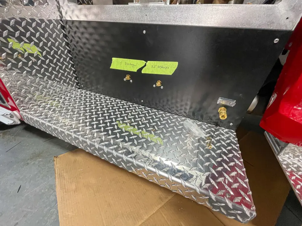 Exterior view of small fire truck showing cab, body compartments, and wheel/tire area.